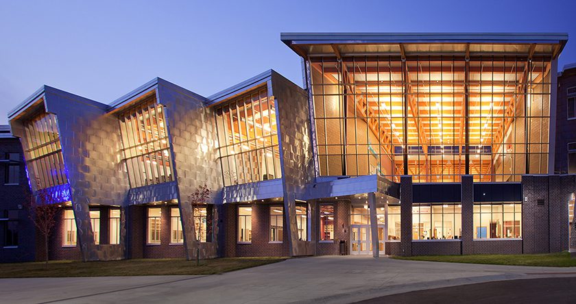 exterior view of school with giant windows with lights on at night