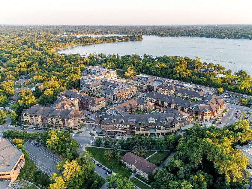 aerial view of housing and retail complex with lake and green trees