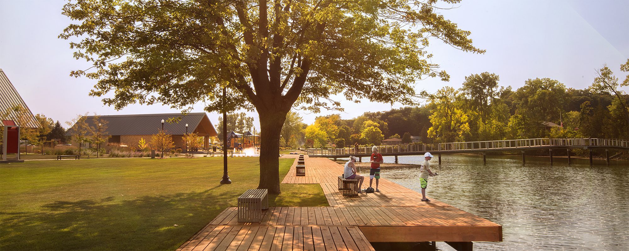 Schematic design showing park with wooden decking, seating, a bridge and mature trees alongside a river