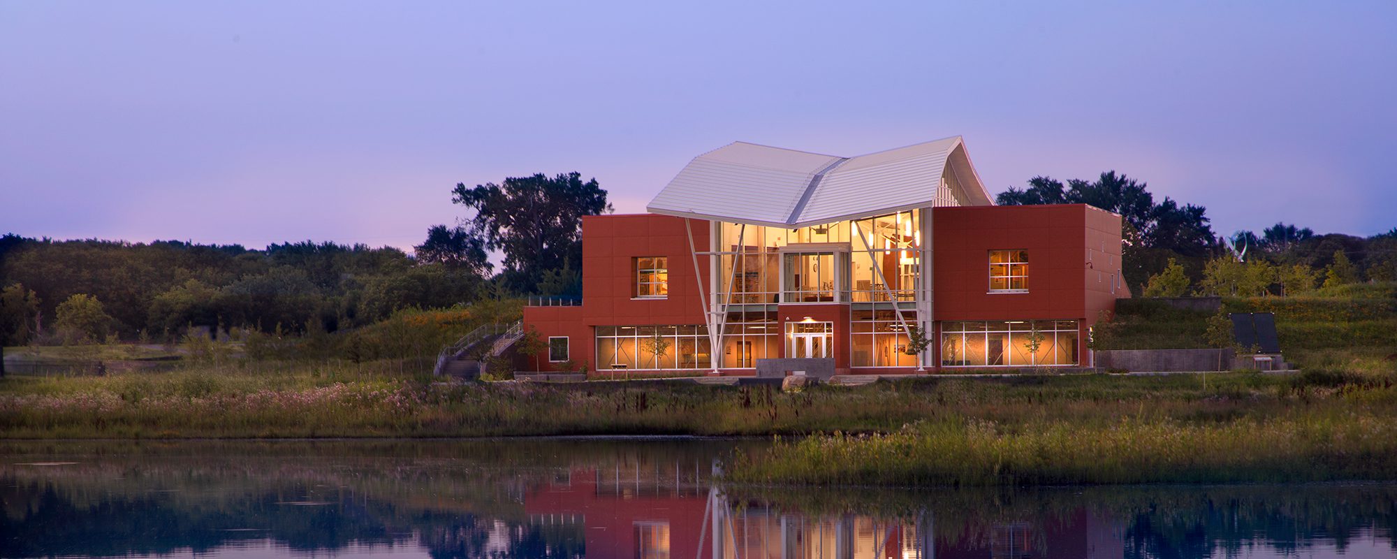 A community center done in contemporary design, with a curved roof and glass front, at dusk