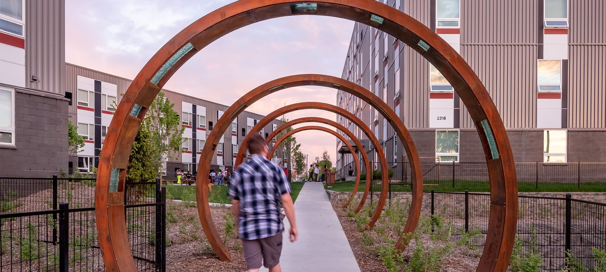 man walking through circular arches near apartment building community courtyard